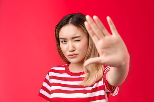 Close-up serious-looking determined asian blond woman pull hand forward show stop taboo sign, concentrating gaze on camera look with one eye, demanding stop, tell enough, say no, red background photo