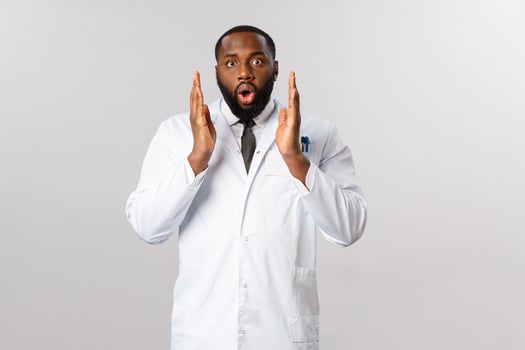 Portrait of young shocked speechless african-american male doctor, physician heard laboratory starts testing covid-19 vaccine, feel astounded and amazed, staring camera startled, grey background photo