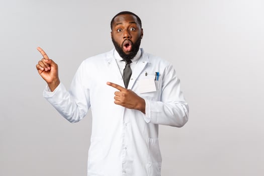Covid19, healthcare and clinic concept. Amazed african-american doctor in white coat gasping impressed seeing incredible news, sharing info about coronavirus pandemic situation, point left photo