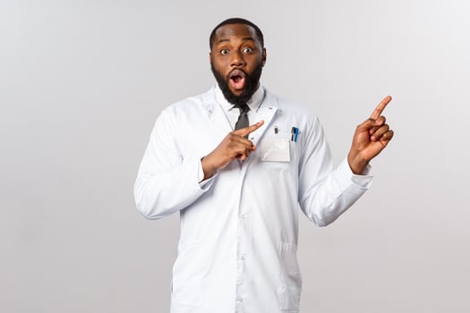 Impressed good-looking male african-american doctor in white coat, pointing upper right corner, gasping and staring camera excited and amazed, tell good news, look its awesome photo