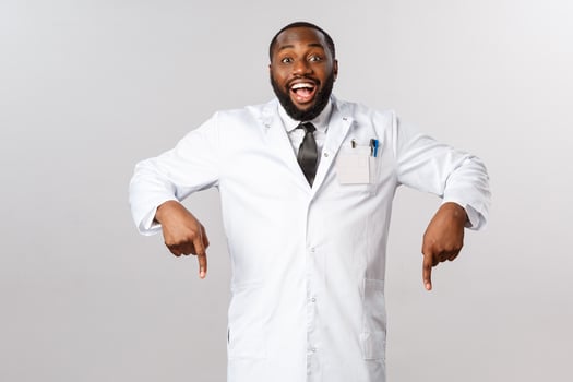 Cheerful excited, happy african-american male doctor inviting see great thing, pointing fingers down, ask to look and check-out awesome product, guarantee best quality, grey background photo