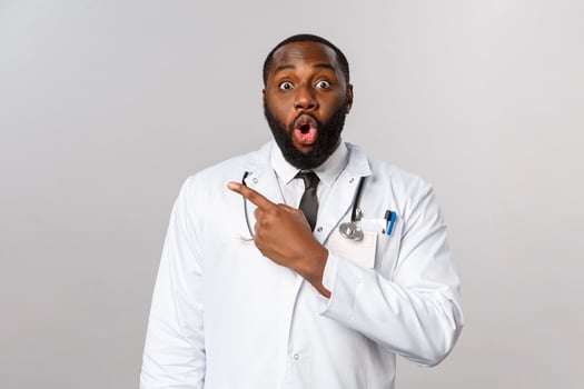 Healthcare, medicine and epidemic concept. Impressed african-american male doctor look with interest at camera as discuss new pills or medication, pointing fingers upper left corner photo