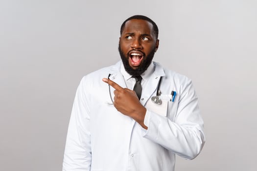 Healthcare, medicine and epidemic concept. Shocked and startled, upset african-american doctor seeing something cringy and shocking, pointing looking upper left corner frustrated photo