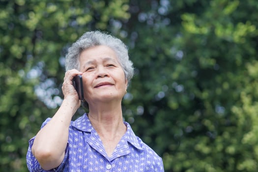 Happy beautiful senior woman is using a smartphone and looking up while standing in a garden. Space for text. Aged people and communication concept photo