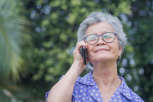 Happy beautiful senior woman is using a smartphone and looking up while standing in a garden. Space for text. Aged people and communication concept photo