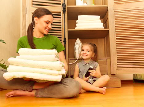 Smiling woman with little daughter sitting near cupboard holding towels in laundry room photo