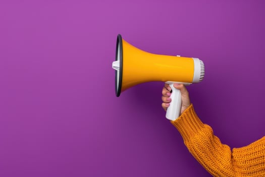 Hand holding a yellow megaphone against a purple background photo