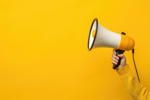 Hand holding a megaphone against a bright yellow background photo