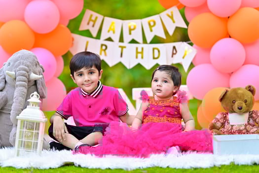 Two children in pink dresses sitting on a blanket with balloons photo