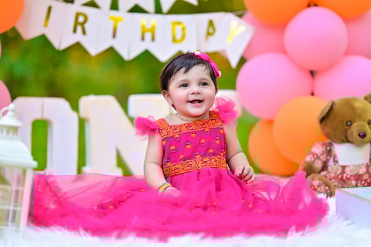 A baby girl in a pink dress sitting on a blanket photo
