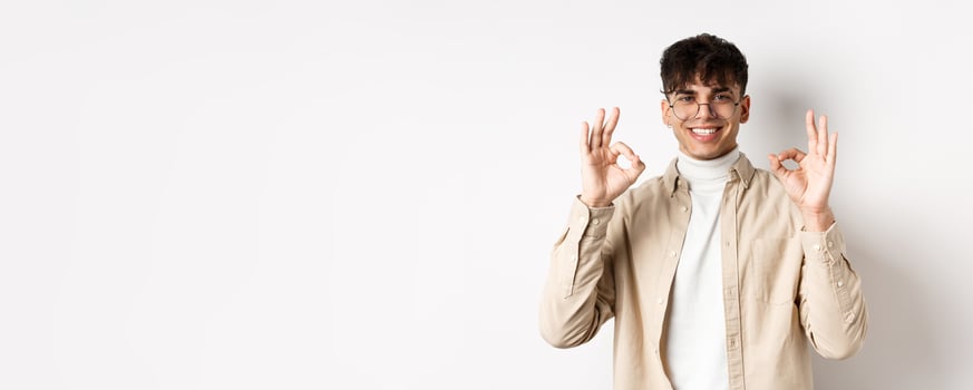 Handsome young man recommending good product, showing okay gestures and smiling, agree or approve something, praising excellent choice, standing on white background photo