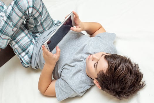 boy lies on his back playing digital tablet photo