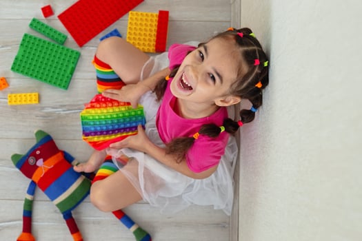 cheerful little brunette girl in bright colorful clothes, sits at home, on the floor photo