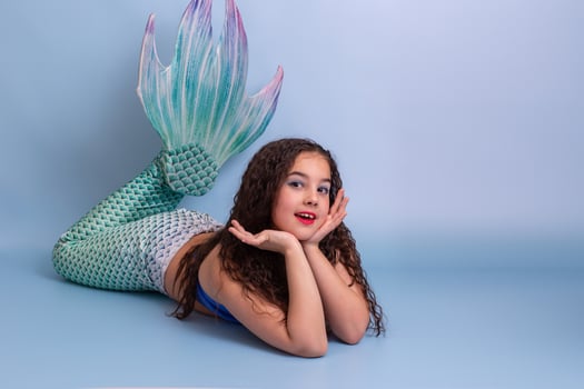 Adorable child girl in a mermaid costume lie isolated on light-blue background photo