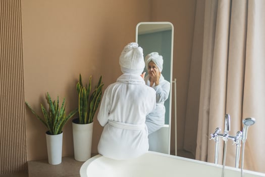 Mature adult old woman looking at mirror applying nourishing anti age face cream doing daily beauty routine. Senior woman with white mask creme on skin gets facial treatment Skin care aging skincare photo