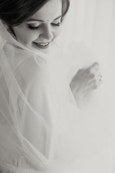 A bride is posing for a picture with her veil pulled back. She is smiling and looking at the camera photo