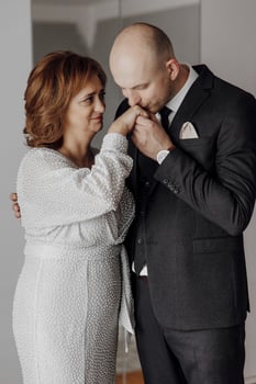 mother hugs her adult son in the room. Mother and son are festively dressed photo