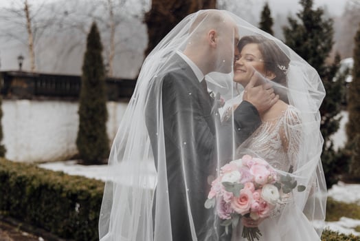A bride and groom are standing under a white veil, with the bride holding a bouquet of pink flowers photo