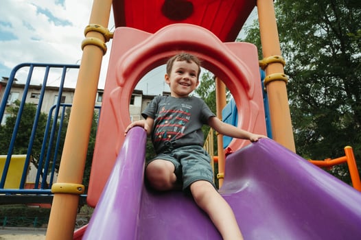 preschooler boy plays on a slide on playground in summer photo