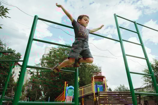 preschooler boy jumps from horizontal bars on playground in summer photo