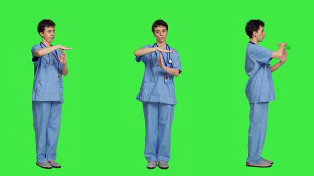Medical assistant giving timeout symbol against greenscreen backdrop, showing limits and asking for a break. Nurse doing pause or stop gesture while she wears blue scrubs. Camera A. photo