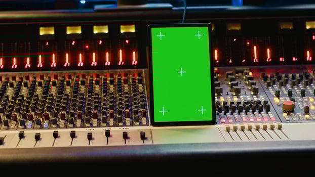 Professional audio expert mixing and mastering tracks in music production studio, pushing buttons and switchers in control room. Sound engineer recording tunes with greenscreen tablet. Camera A. photo