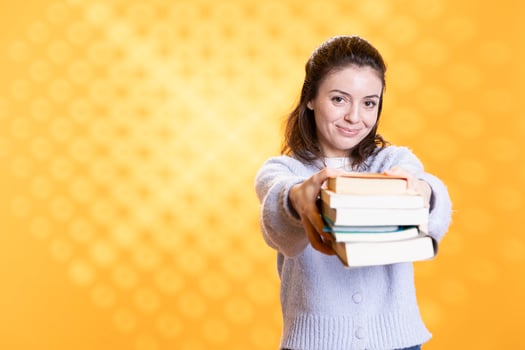 Portrait of friendly woman offering stack of textbooks useful for school exam, isolated over studio background. Merry person giving pile of books, recommending them for university assessment photo
