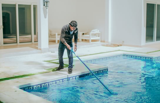 Man cleaning swimming pool with a suction hose. Worker cleaning a home pool with a vacuum hose photo