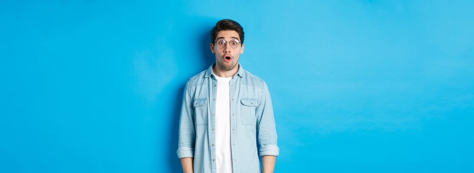 Surprised man in glasses looking at promo offer, saying wow amazed, standing over blue background photo