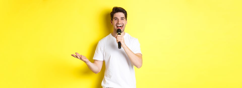 Happy man entertainer performing, talking in microphone, making speech or stand-up show, standing over yellow background photo
