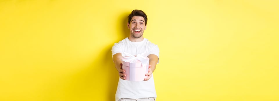 Concept of holidays and celebration. Smiling man giving you gift, congratulating, standing over yellow background with present photo