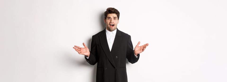 Portrait of confused and worried handsome man in suit, looking at something strange, spread hands sideways and standing puzzled against white background photo