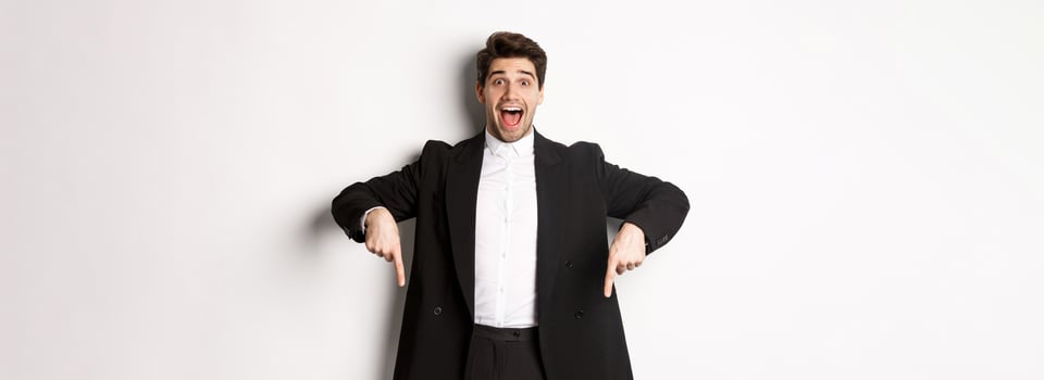 Portrait of super happy man showing christmas promo offer, pointing fingers down and smiling amazed, wearing formal party suit, standing over white background photo
