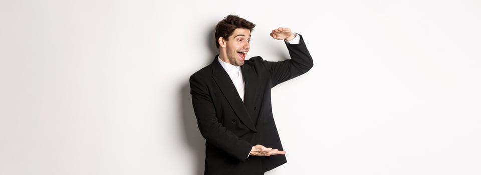 Portrait of excited handsome man in suit, shaping big object on copy space and smiling amazed, holding something, standing over white background photo