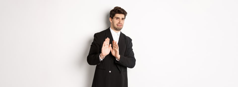 Image of stylish handsome man in black suit, cringe from something embarrassing, declining offer and showing stop gesture, standing against white background photo