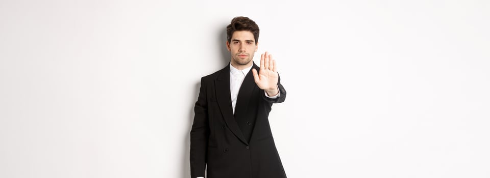 Portrait of serious handsome man in formal suit, extending hand to stop you, prohibit action, forbid and disagree with something, standing against white background photo