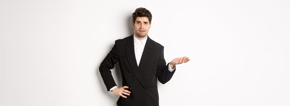Image of confused handsome man in formal suit, raising hand and shrugging, cant understand something, standing against white background photo