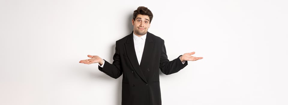 Image of handsome confused man in black suit, shrugging and looking clueless, dont know anything, standing over white background photo