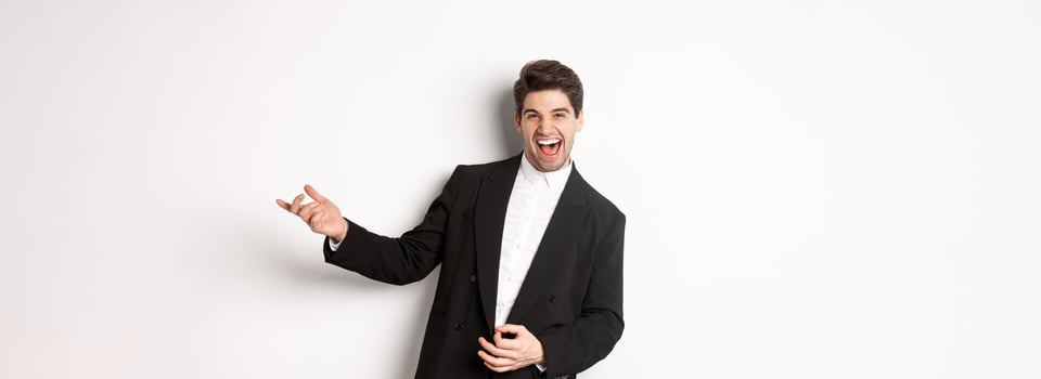 Portrait of happy man dancing at party, playing on invisible guitar and laughing, standing in black suit against white background photo