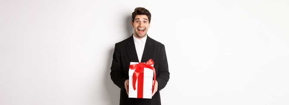 Concept of christmas holidays, celebration and lifestyle. Image of handsome guy in black suit looking excited, have a gift, standing against white background photo
