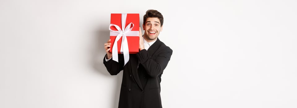 Handsome man in black suit, receiving christmas gift, smiling amazed, standing against white background photo