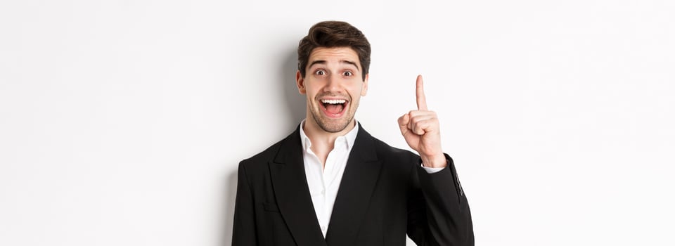Close-up of handsome businessman in black suit, smiling amazed, showing number one, standing over white background photo