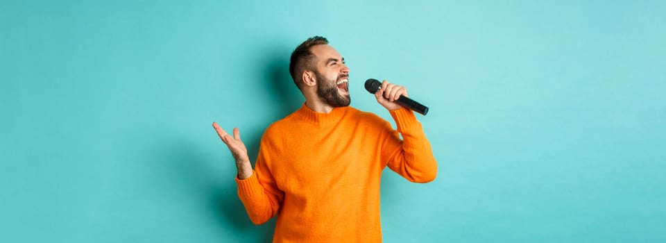 Handsome adult man perform song, singing into microphone, standing against turquoise background photo