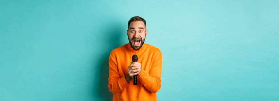 Handsome adult man perform song, singing into microphone, standing against turquoise background photo