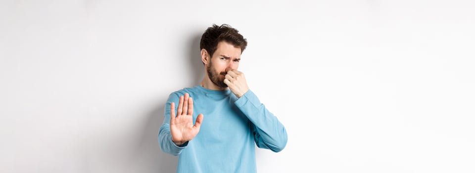 Image of caucasian man stretch out hands to stop or reject something, shut nose disgust, refusing product with bad smell, standing over white background photo