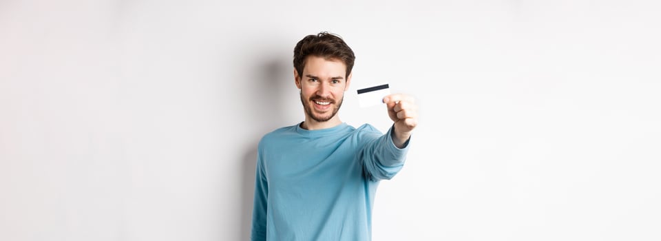 Confident young man smiling, stretch out hand and showing plastic credit card, standing on white background photo