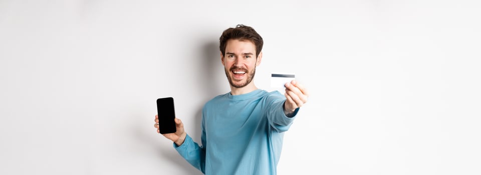 E-commerce and shopping concept. Happy man showing plastic credit card and screen of smartphone, recommending banking app, standing on white background photo