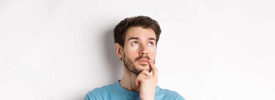 Face of young caucasian man looking up pensive, making choice or thinking, pondering while standing over white background photo
