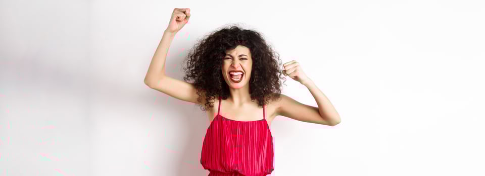 Cheerful emotive woman with curly hair, red dress, raising hands up and chanting, rooting for team, shouting wanting to win, standing on white background photo