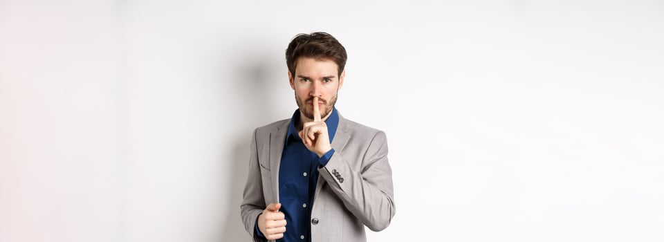 Angry businessman showing taboo sign, shushing and tell to keep quiet, need silence, standing with finger on lips and looking at camera, white background photo